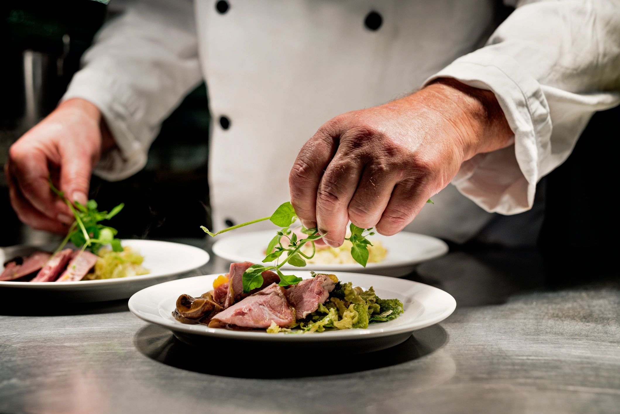 Chef adding pea shoots to a plated dish at a restaurant pass